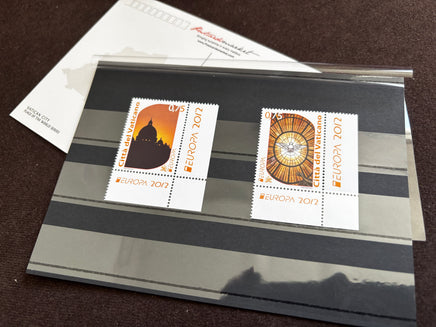 Two vintage 2012 European Union postage stamps mounted on a clear plastic sleeve, displayed on a dark striped card over a white envelope.