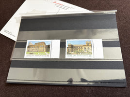Two Vatican City postage stamps displayed side by side on a black-and-white striped protective sleeve, with part of a white envelope visible at the top left on a dark brown surface.