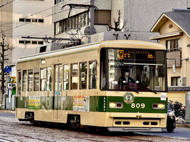 Beige tram with green accents on a city street in Japan