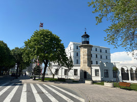 Lighthouse-like building with a clock tower in a town square with trees and benches.