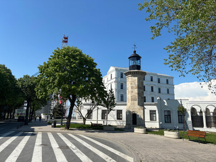 Lighthouse-like building with a clock tower in a town square with trees and benches.