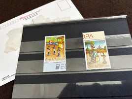 Two vintage Italian 'Città del Vaticano' postage stamps displayed side-by-side on a black striped protective plastic sleeve, with a white stamp envelope partially visible behind them.