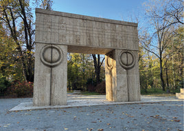 Large stone archway in a park with trees and clear sky